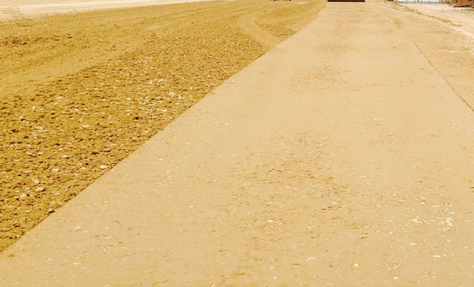 A smooth, sealed section of road base beside a strip of loose, untreated material
